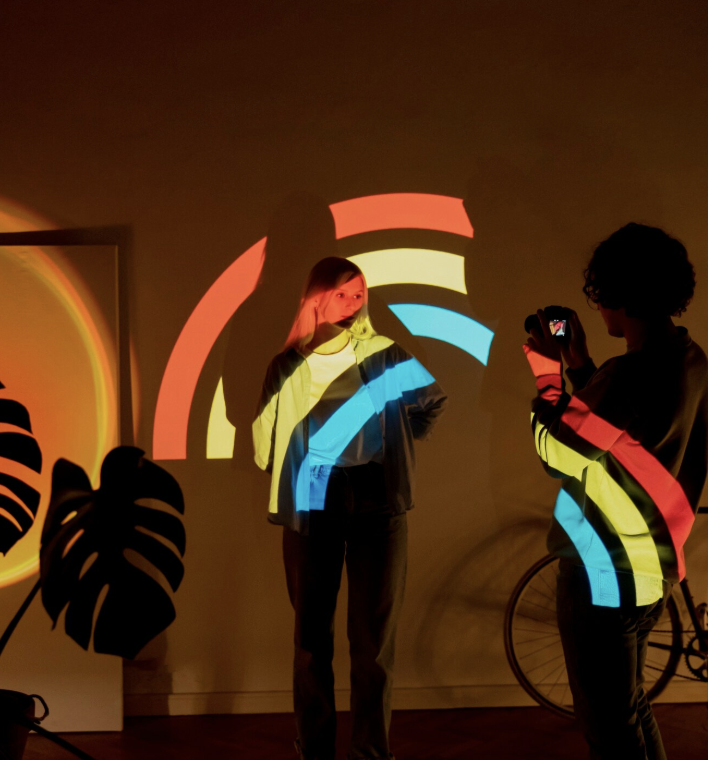 Mujeres proyectadas con luces de arcoíris en un ambiente artístico, reflejando diversidad, empoderamiento y cultura pop contemporánea.
